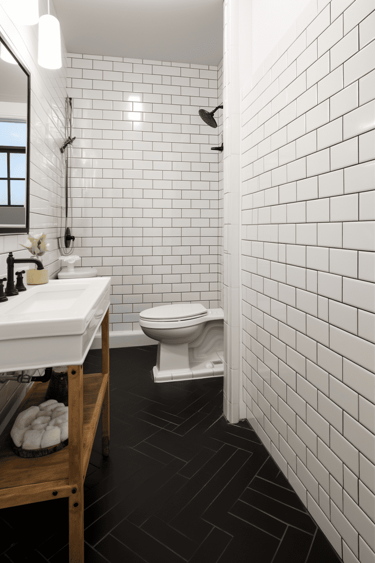 A bathroom with bright white subway tile paired with black grout and solid black tile for the floor. 
