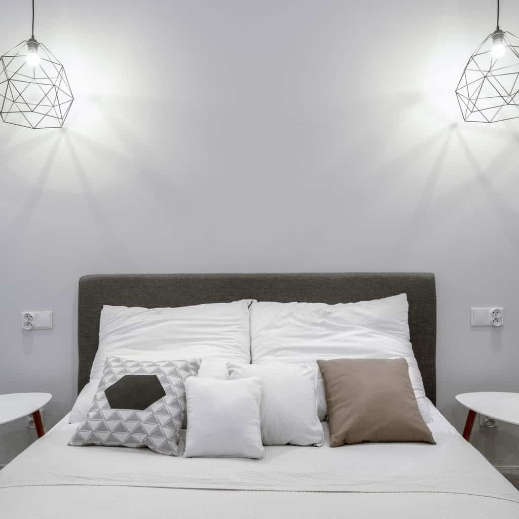 A headboard with white beddings, gray headboard, and two hanging industrial themed lamps