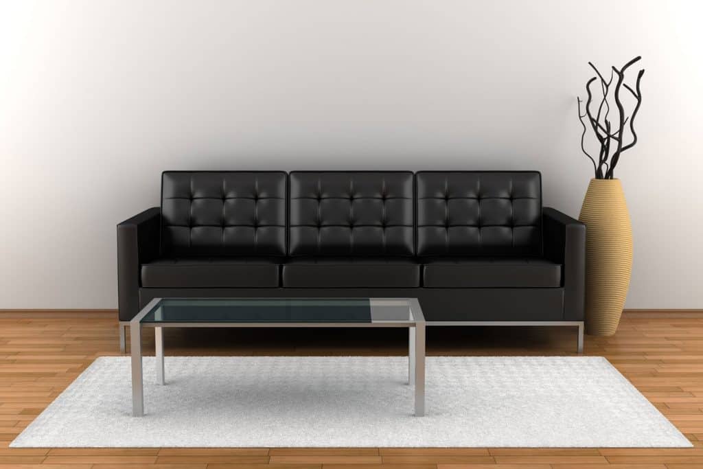 A black colored square arm sofa with a metal framed glass coffee table above a white rug