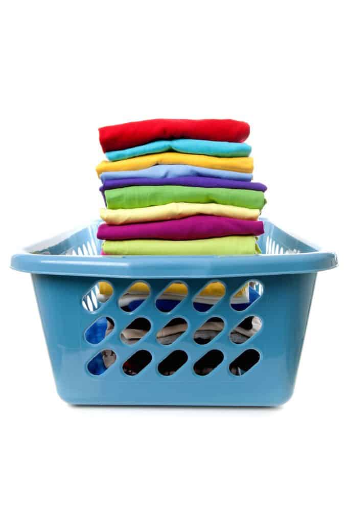 A blue laundry basket filed with folded clean t-shirts