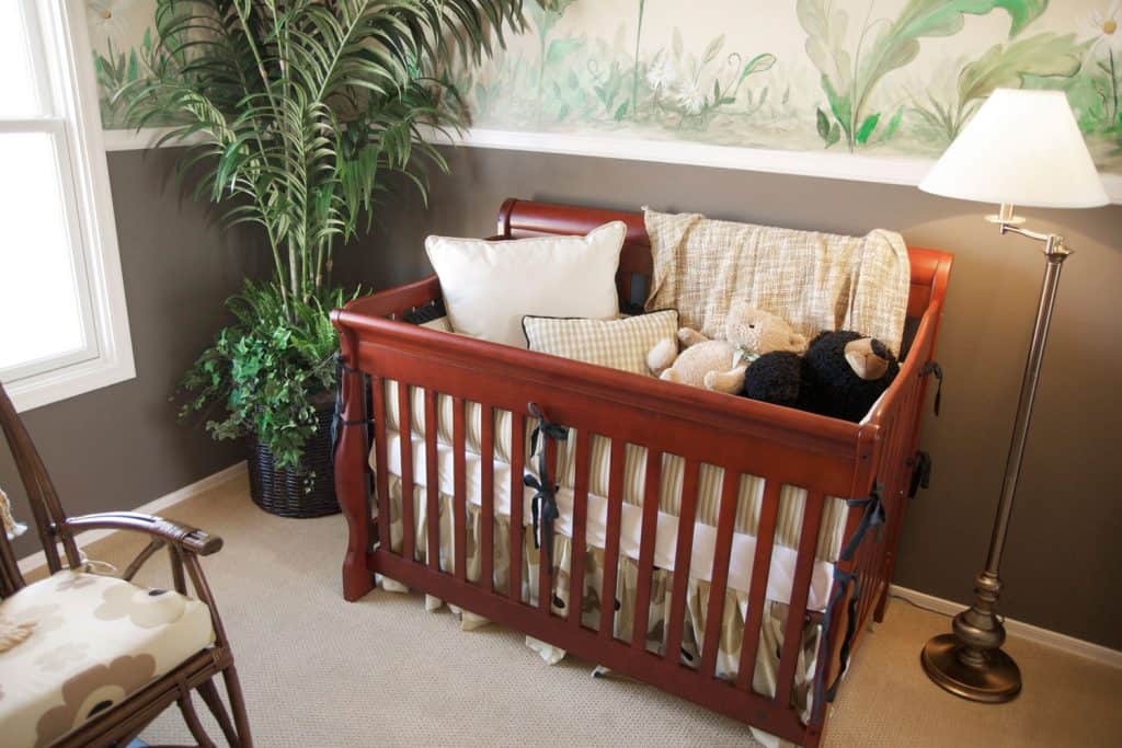 A cherry maple wood crafted babies crib with pillows and teddy bears