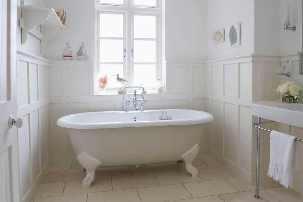 A classic themed bathroom with an old fashioned bathtub, and a French window on the background
