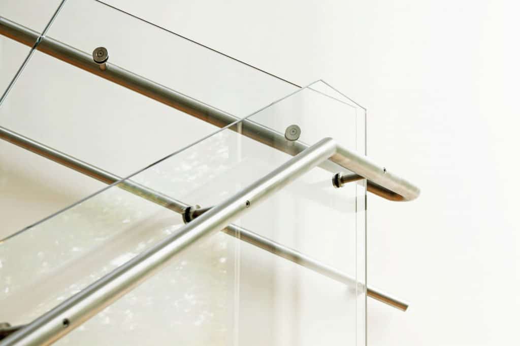 A glass wall of a staircase with stainless steel metal railing