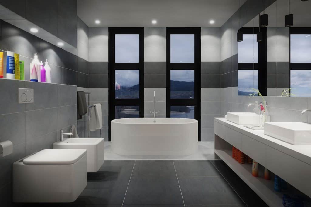 A gray and white themed bathroom with vertical windows, two luxurious toilet seats, and a large vanity area with a huge window