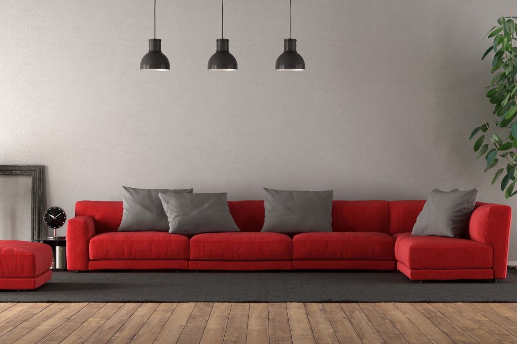 A gray area rug with a red sectional couch with gray throw pillows on it