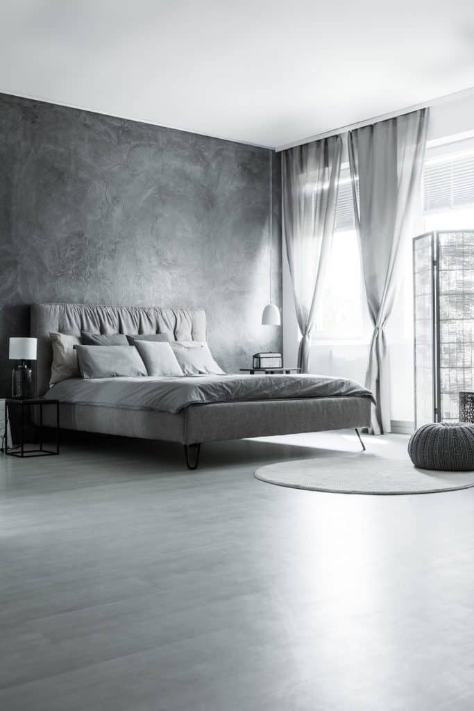 A gray themed bedroom with a huge window on the right and a bed with gray beddings