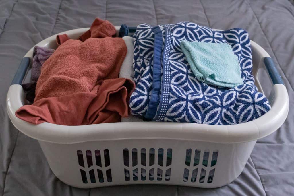 A laundry basket filed with laundry on a bed