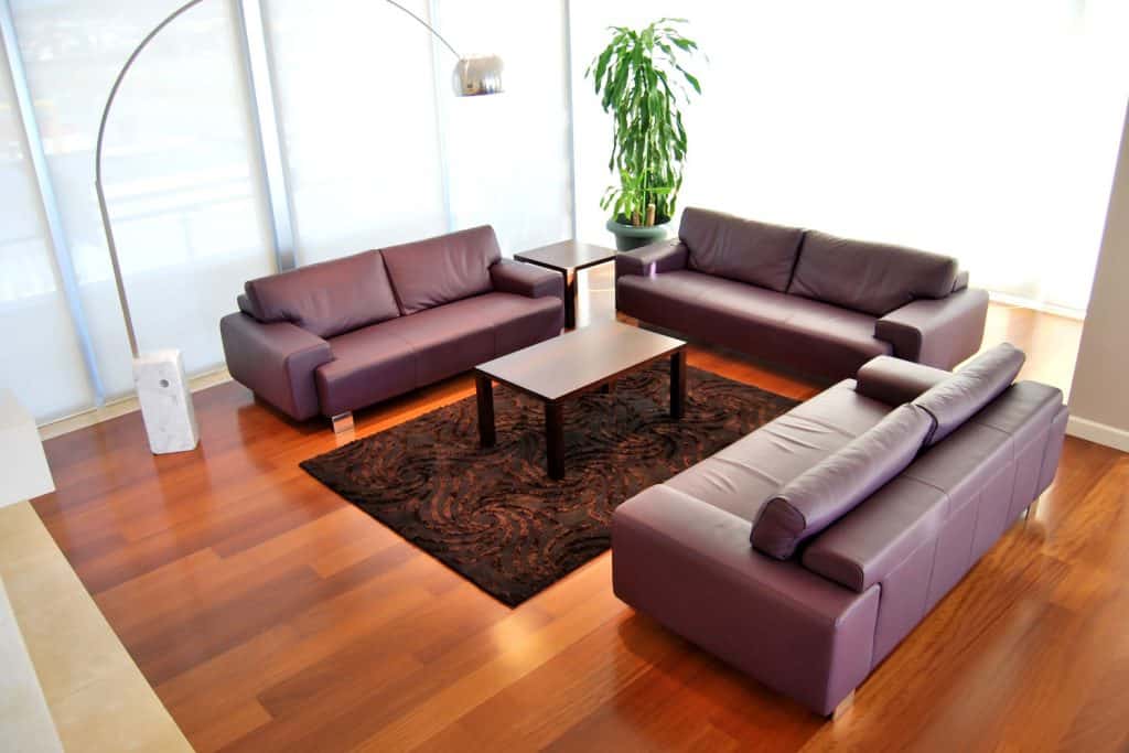 A minimalist themed living room with brown couches, dark brown rub and a wooden laminated flooring