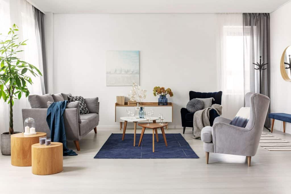 A modern bohemian themed living room with gray couches, blue rug, and wooden furniture's inside a white walled living room 