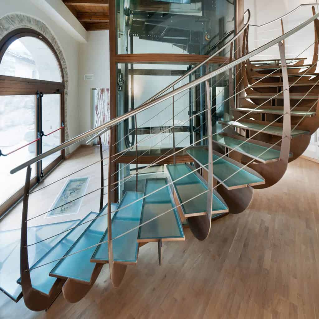 A modern glass winding staircase with glass steps and metal framed railings