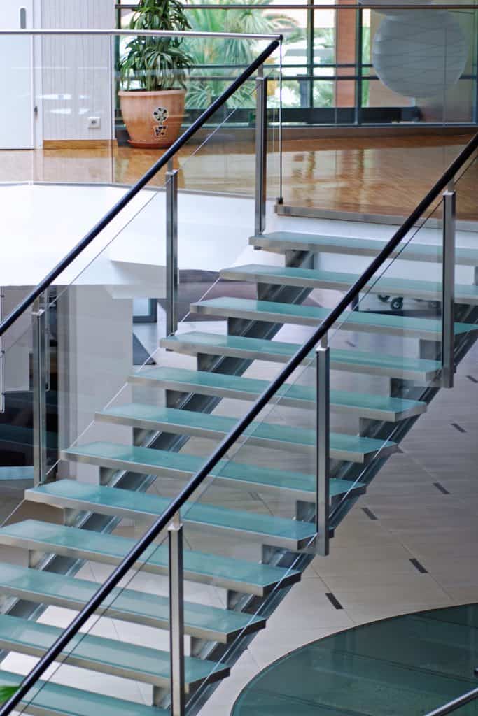 A modern staircase with a glass stair steps, metal framing, and a tempered glass wall