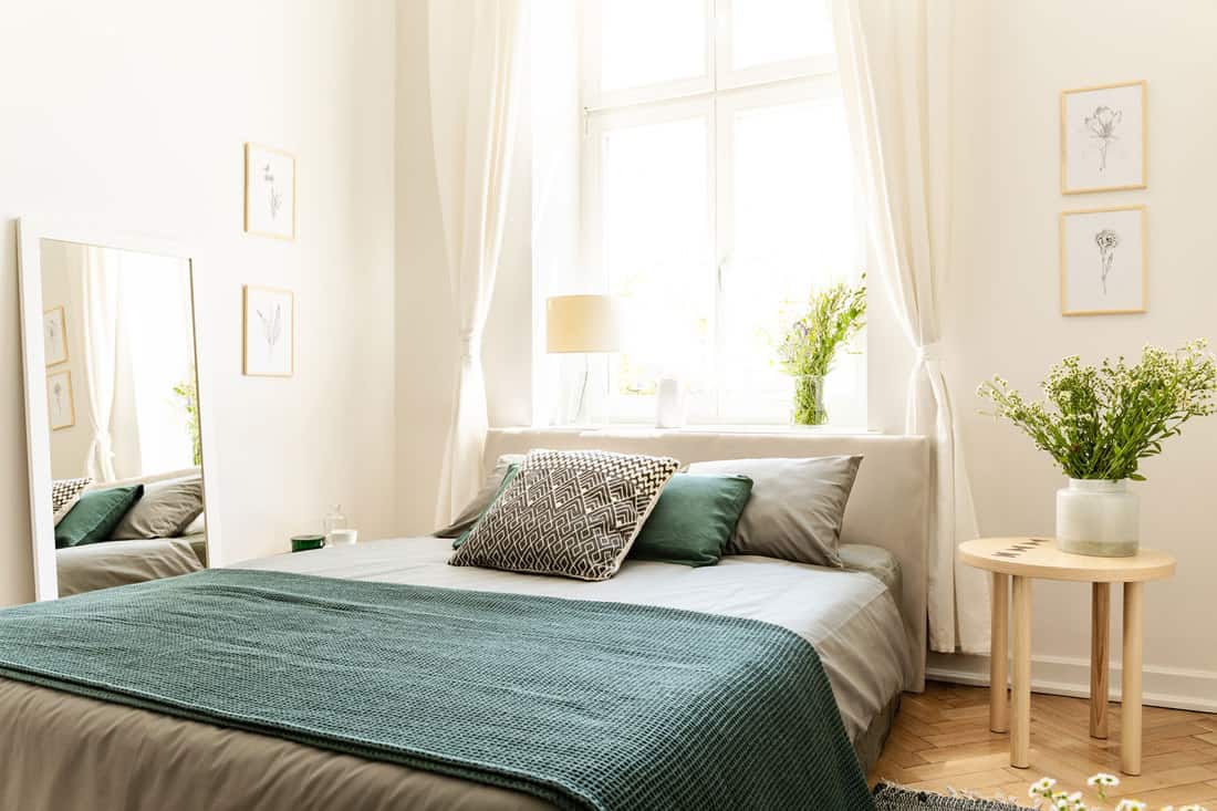 Modern well lit bedroom with a classic bed, white and teal colors, and indoor plants, What Color Bedding Goes With Cream Walls?