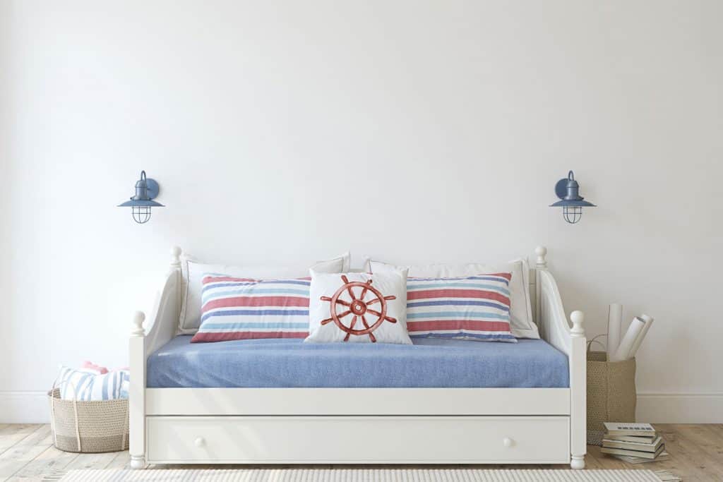 A nautical themed living room with a sofa, blue beddings and an off white colored wall