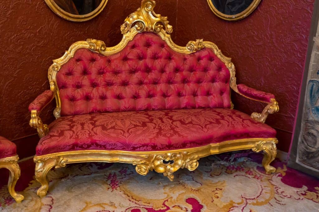 A royal loveseat with gold plated molding and a red leather covered foam with floral design