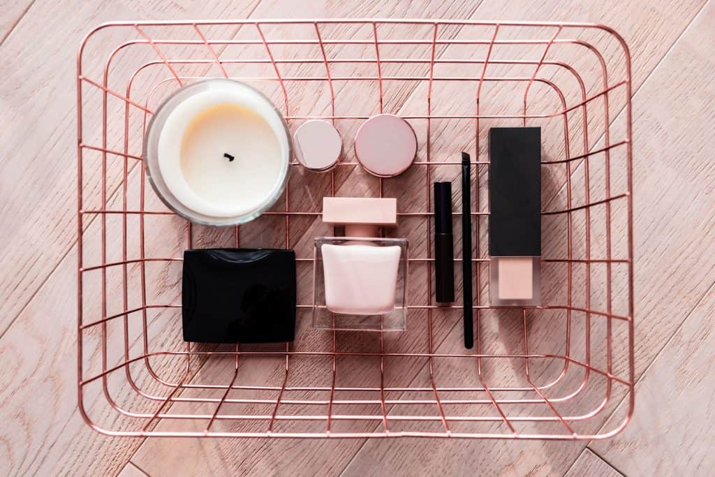 A small basket with make up, lipstick, blush-on and a scented candle on the side