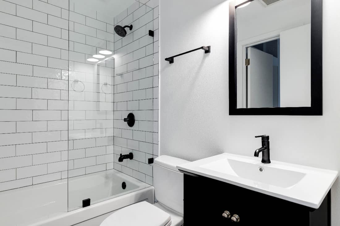 A small modern bathroom with a dark vanity, mirror frame, and hardware