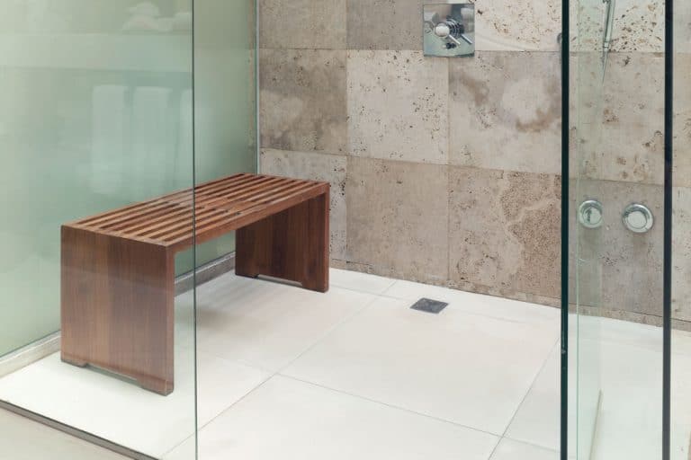 Small wooden shower bench inside a modern white and faux tiled bathroom, Best Shower Benches For Small Shower [4 Types Inc. Examples]