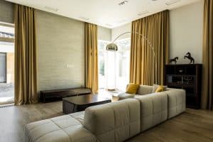 Spacious living room with a wooden vinyl flooring, yellow curtains, huge windows and a sectional sofa with a black coffee table, Should Curtains Match In An Open Floor Plan?