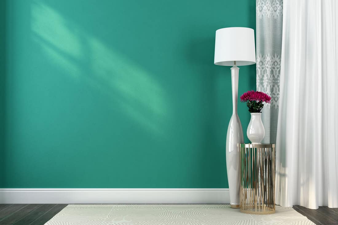 A teal green wall with a white curtain on the side and gray flooring with white rug