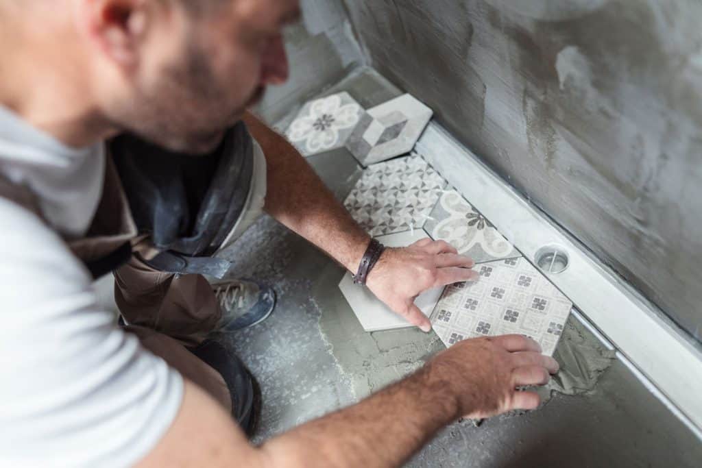 A tile setter properly placing patterned tiles on the side of a bathroom
