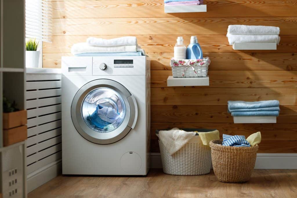 A washing machine and laundry baskets filed with laundry inside a wooden paneled living room