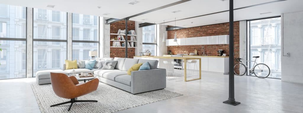 A white modern minimalist themed living room apartment with a gray sectional couch, a small rug and wooden backsplash kitchen area