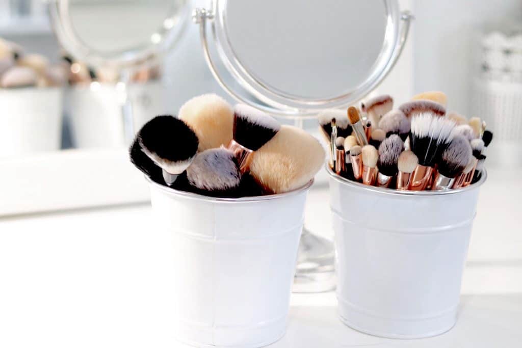 White small buckets filled with brushes for make up and a small round mirror on the background
