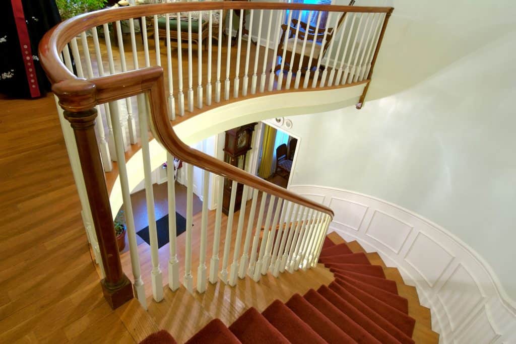 A winding staircase with a carpeted flooring, white painted banisters, and a wooden railing