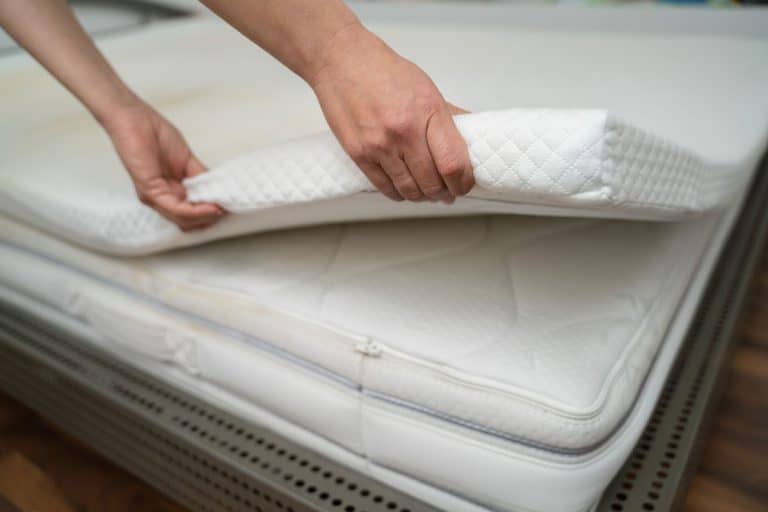 A woman putting on a mattress topper on her room, 7 Types of Mattress Toppers [and How To Choose The Best One]