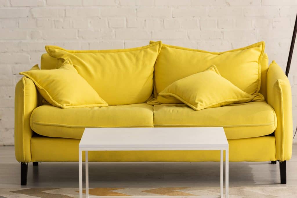 A yellow loveseat with a white coffee table on the front