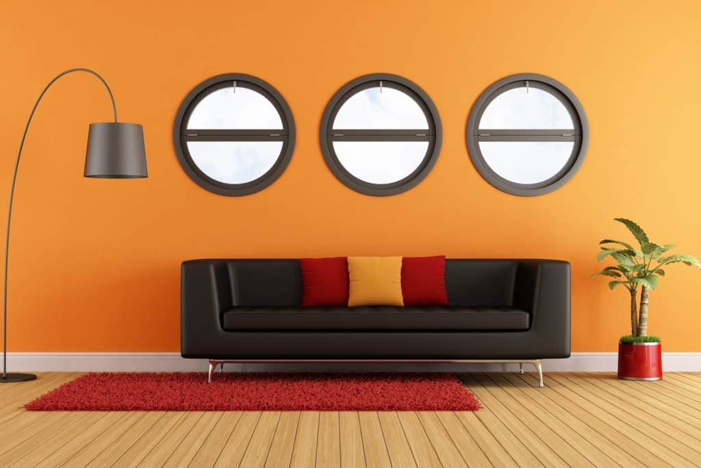 An orange painted living room with a black sofa, red and orange throw pillows, and a red rug
