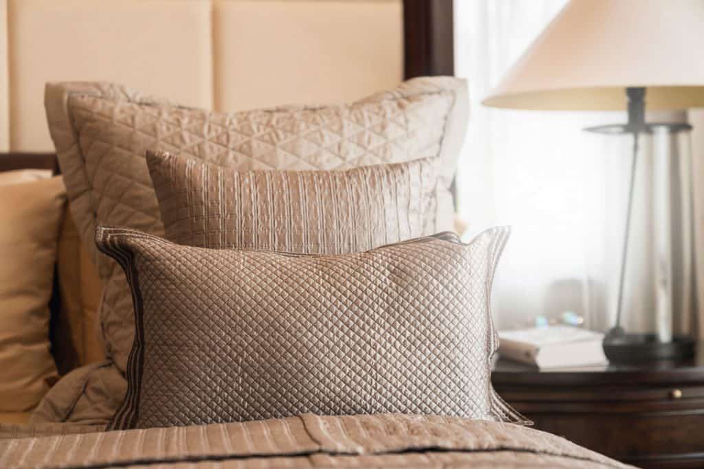 An up close photo of a beige colored bed pillow and a bed with gray headboard