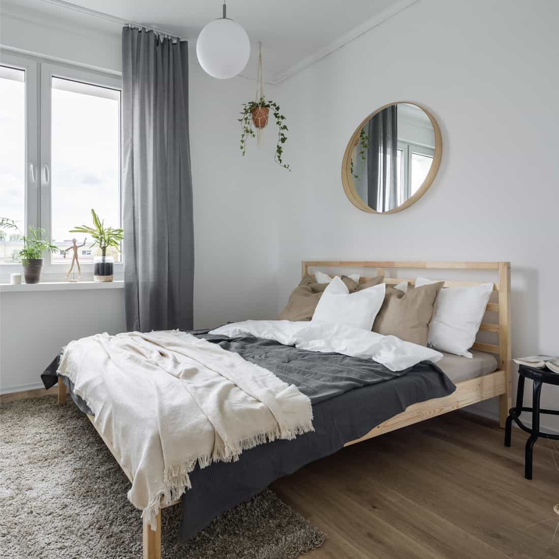Bedroom interior with wooden bed, gray window curtains and mirror