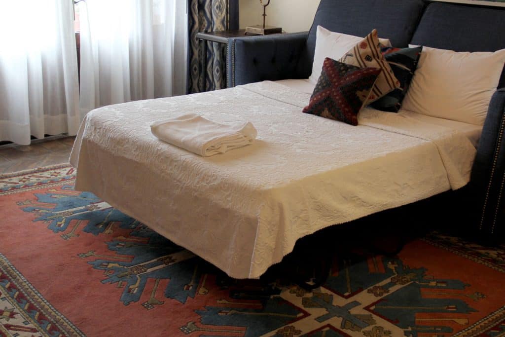 Bedroom with a red patterned carpet, a bed with cream beddings, and a gray headboard