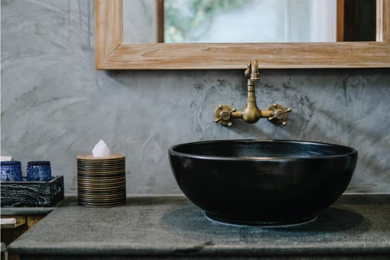 Black sink, vintage copper faucet, gray wall and mirror in loft bathroom, 18 Bathroom Faucet Styles (By Finishes, Handle Options, & Installation)