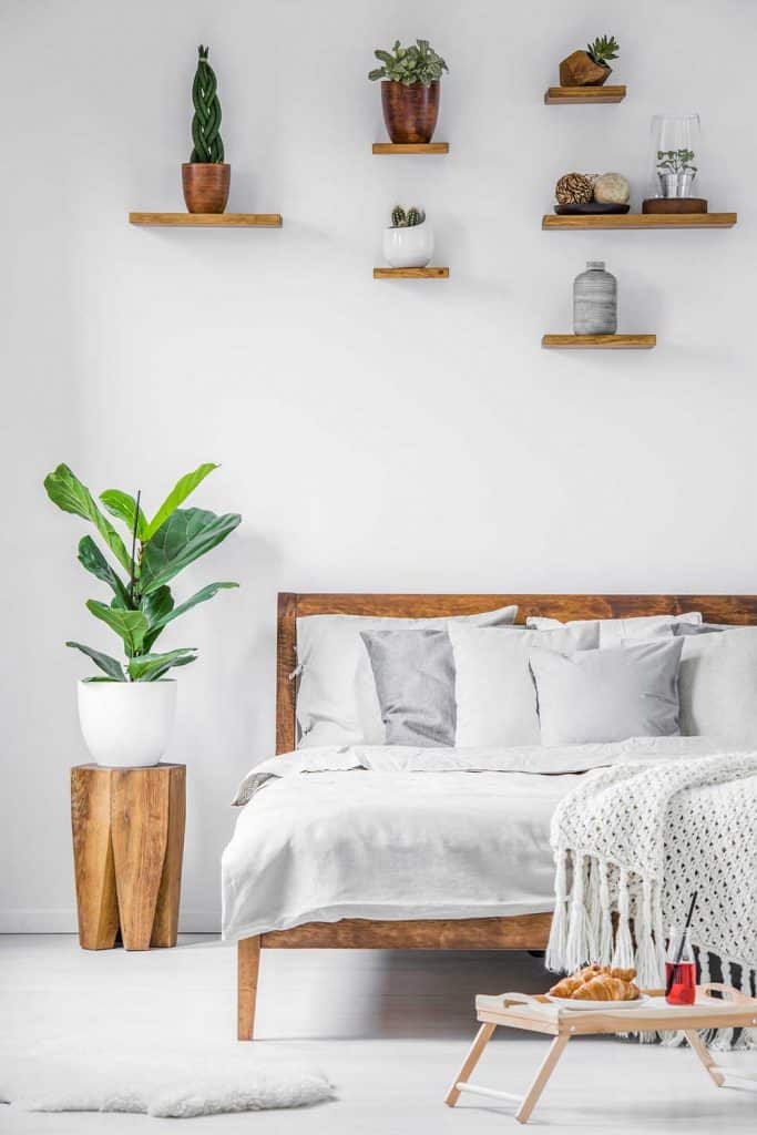 Breakfast tray standing on the floor beside a big comfortable bed with linen, blanket and pillows in a white bedroom interior