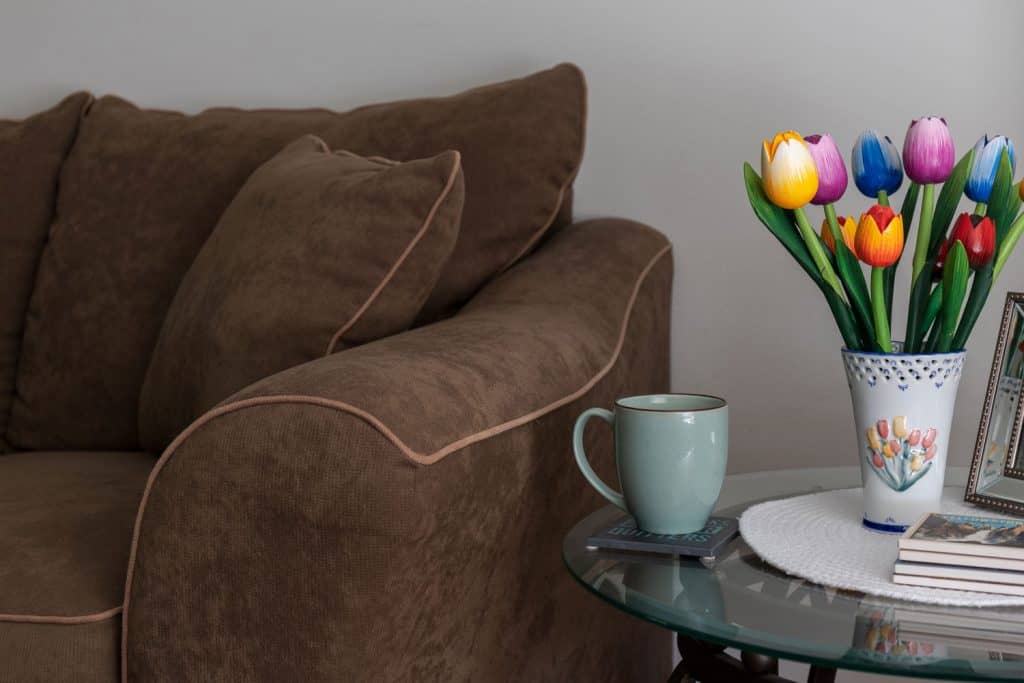 Brown velvet sofa with an end table on the side and beautiful multicolored tulips for decoration