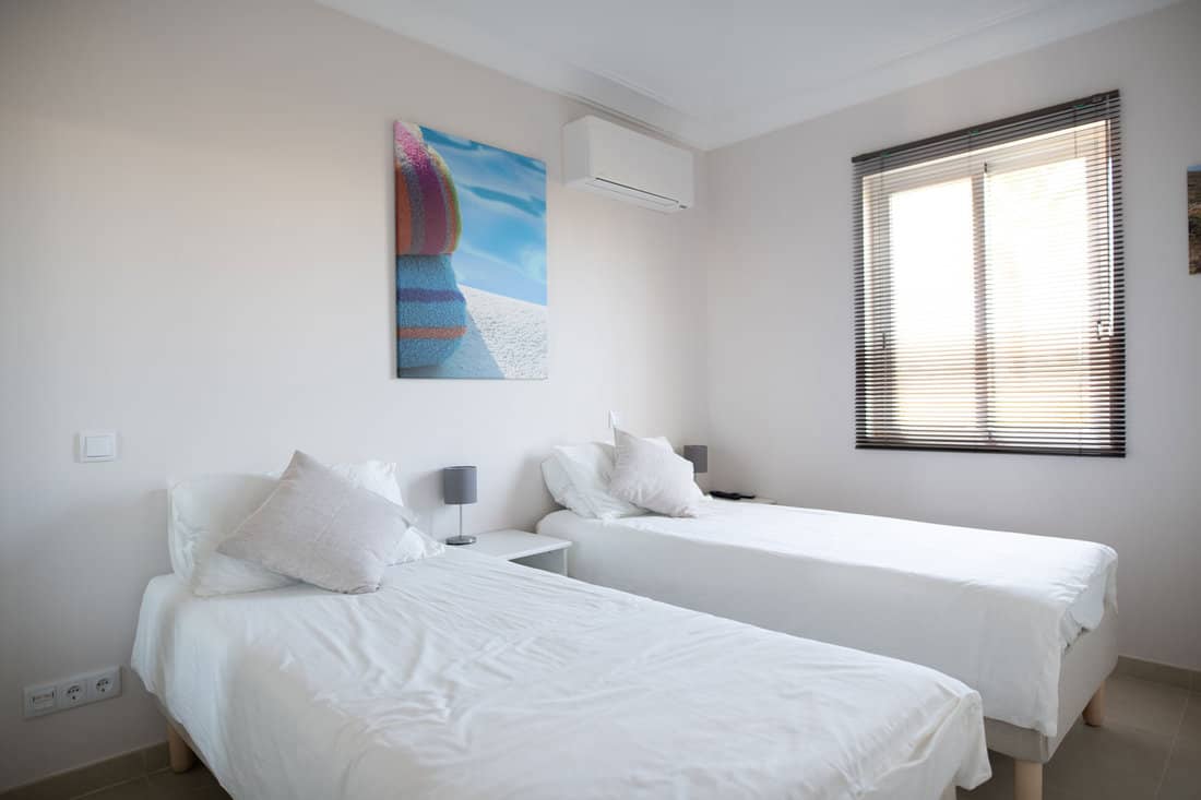 Clean twin bedroom in a house with white bed linen and white walls 