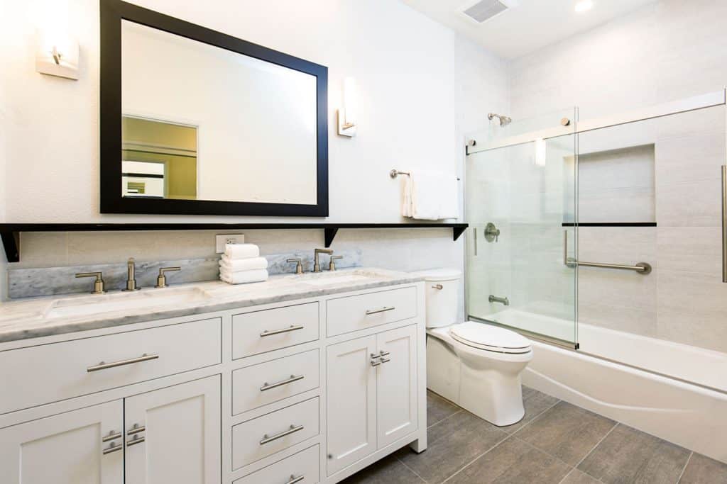 Contemporary bathroom design with white paneled cabinets, his and hers bathroom vanity, and a glass walled bathtub