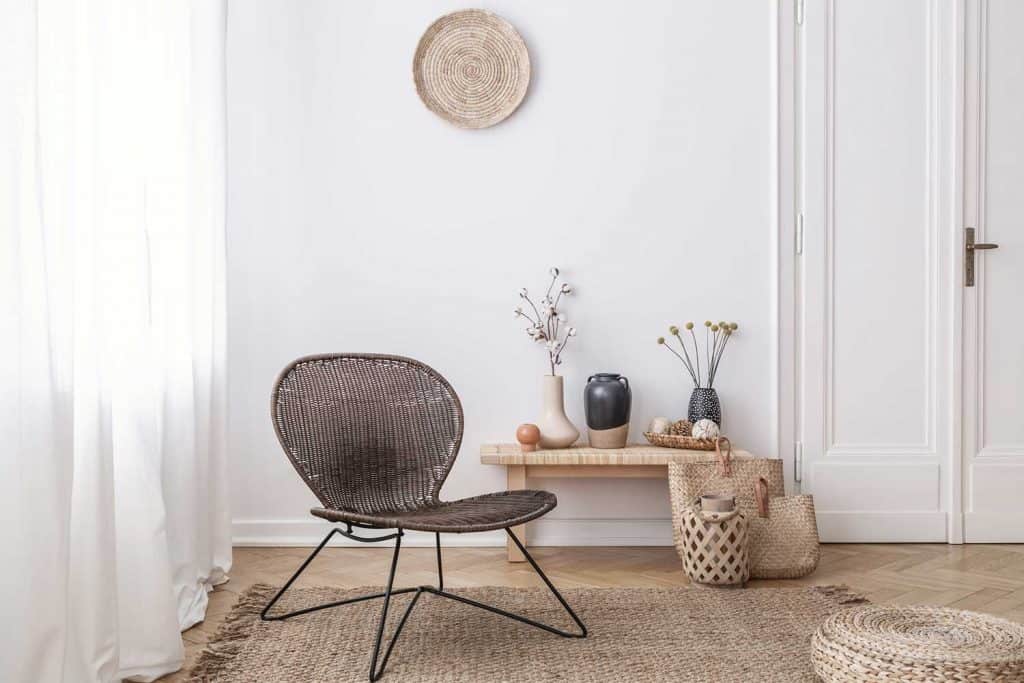 Dark, modern wicker chair in a white living room interior with a wooden bench and decorations made from natural materials