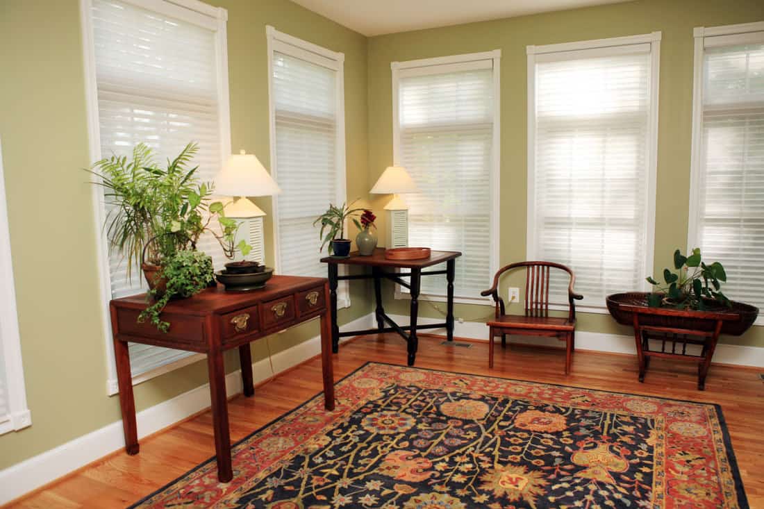End tables, small wooden chair, laminated flooring with a floral rug, and light green walls and windows