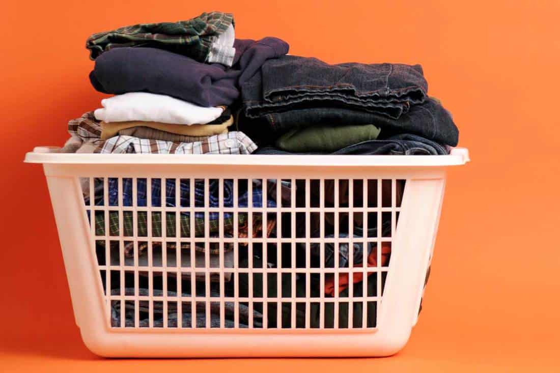 Folded men's clothing in a laundry basket on an orange background, Why Do Laundry Baskets Have Holes?