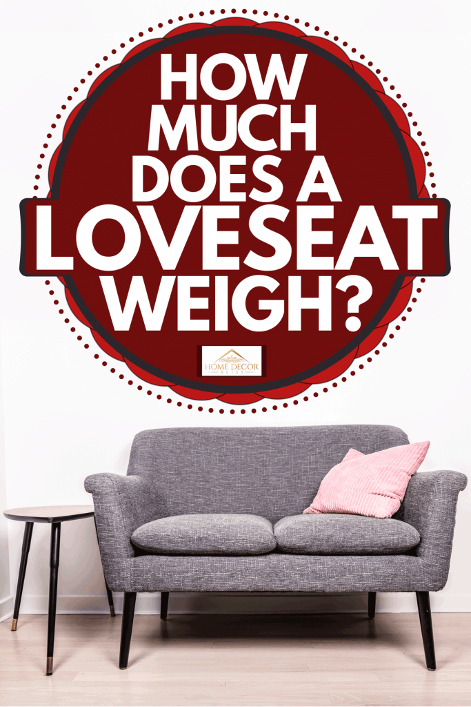 A gray loveseat with a pink throw pillow, and a small bar stool on the side inside a white living room, How Much Does a Loveseat Weigh?