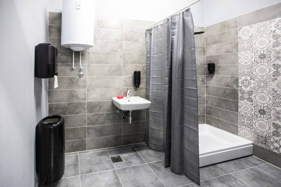 Interior of clean bathroom with sink, shower, shower curtain, boiler and hand dryer