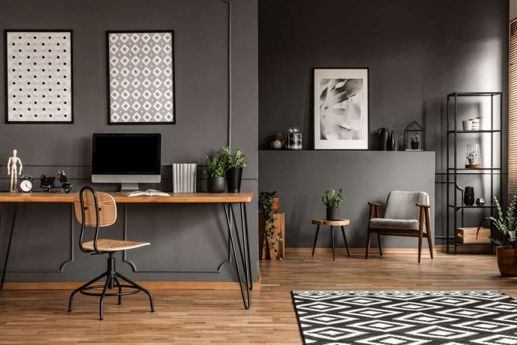 Laminated flooring inside a home office with dark tables, black wall and black and white patterned rug