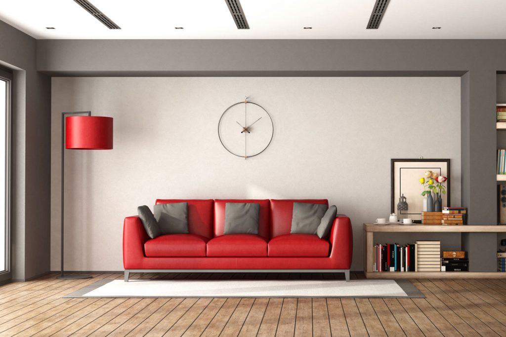 Living room with a red couch, wooden flooring, and a light gray accent wall