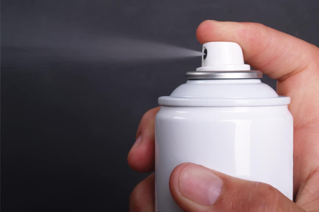 Macro of hand holding generic aerosol can spraying