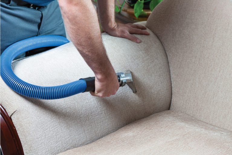 Man cleaning couch with steam cleaner at home, How To Steam Clean A Couch (6 Steps)