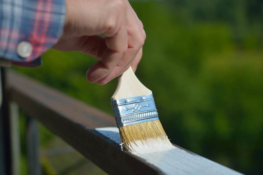 Man painting the handrail with white paint