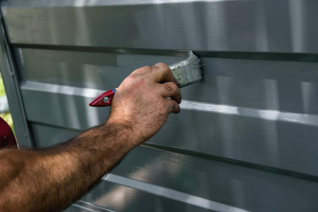 Man painting the metal wall with grey paint